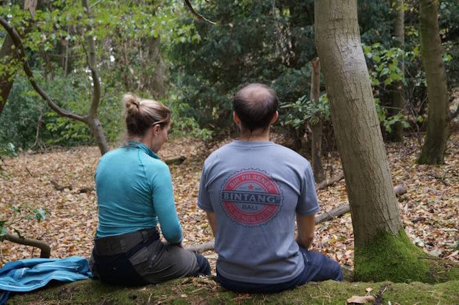 Liz Cramp talking to a patient while sitting on a log in a forest